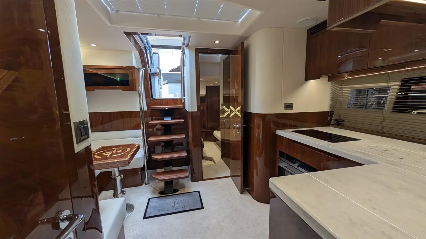 Luxurious yacht interior featuring a kitchen, dining area with a wooden table, and stairs leading to upper deck.